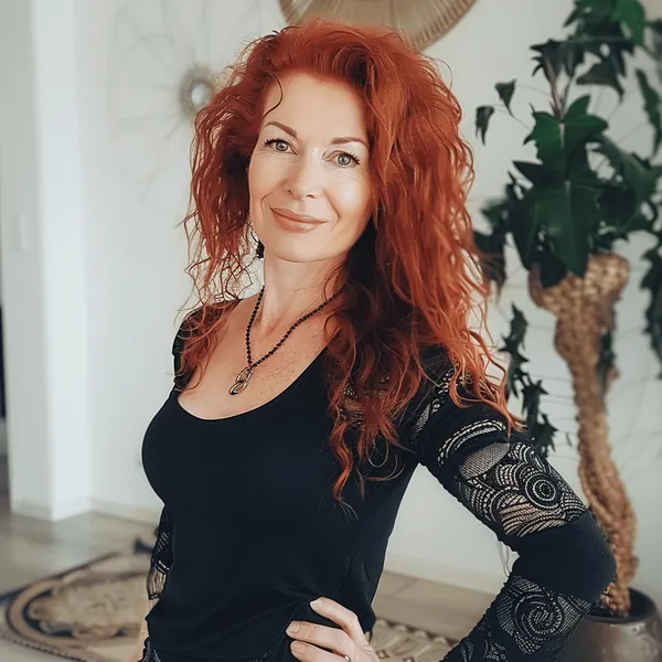 Frau mit voluminösen roten Haaren in einem schwarzen Oberteil, Hand an der Hüfte.